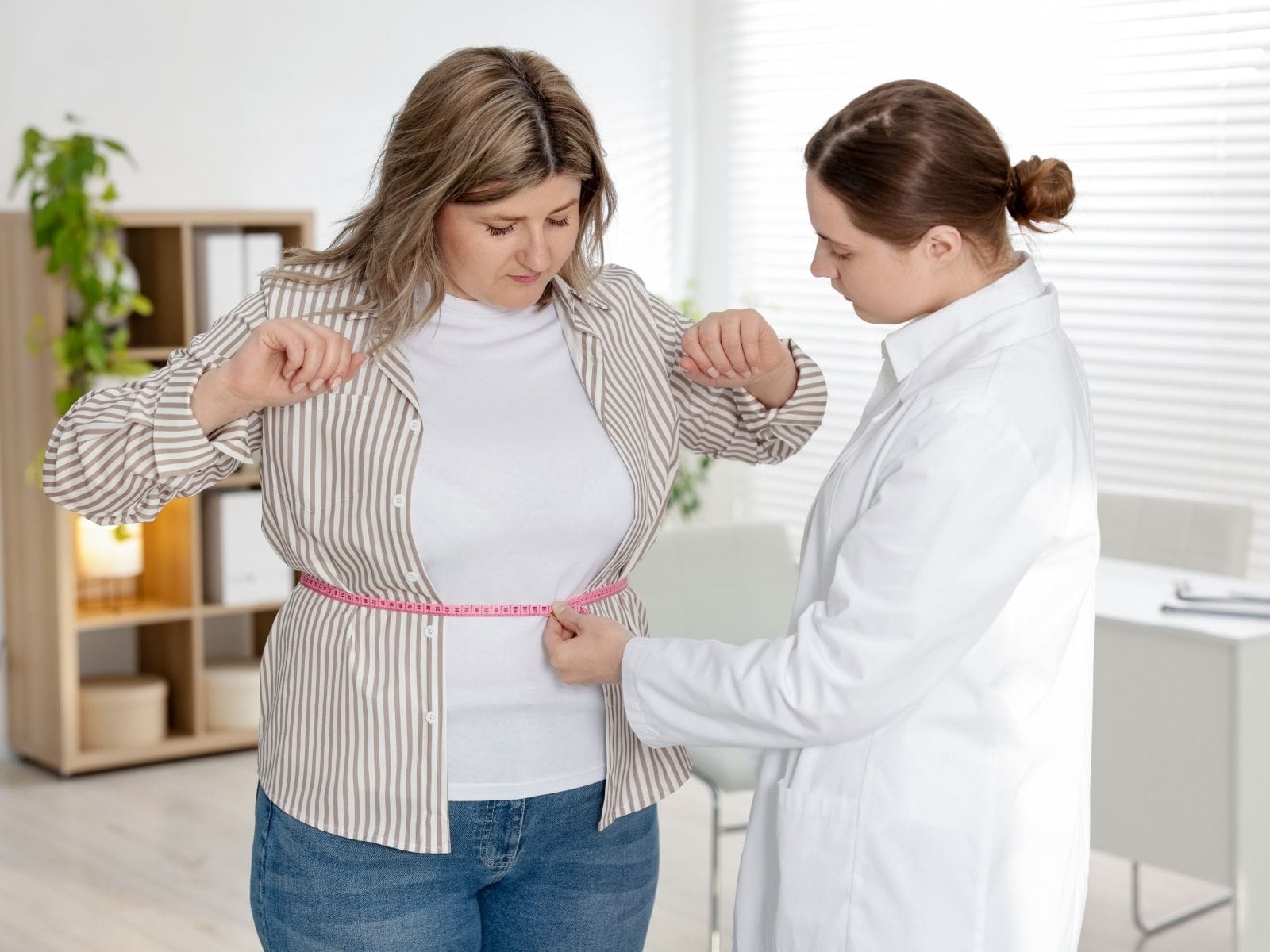 Doctor measuring woman’s waist with tape during weight loss consultation.